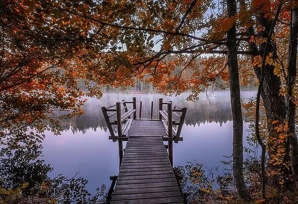 Beautiful fall colors with wooden pier and peaceful lake at autumn morning in Finland