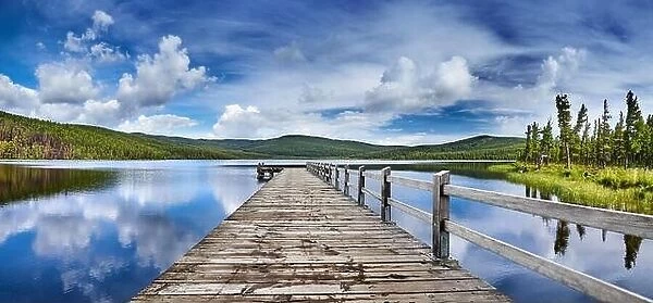Beautiful mountain lake with reflection and wooden pier. Fluffy white clouds and blue sky reflected in still water