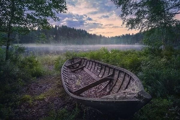 Beautiful sunrise in tranquil lake at summer evening in Finland with wooden boat