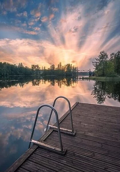 Beautiful sunset in tranquil lake at summer evening in Finland with pier