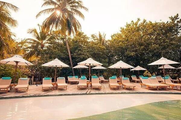 Beautiful tropical beach at resort hotel island. Poolside with chairs, lounger under umbrella and palm trees. Summer holiday, vacation travel concept