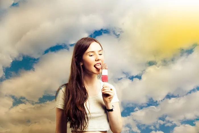 Framed Print : Beautiful young woman licking popsicle against cloudy sky