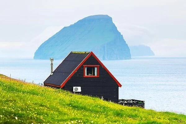 Black house on famous faroese Witches Finger Trail and Koltur island on background. Sandavagur village, Vagar island, Faroe islands, Denmark