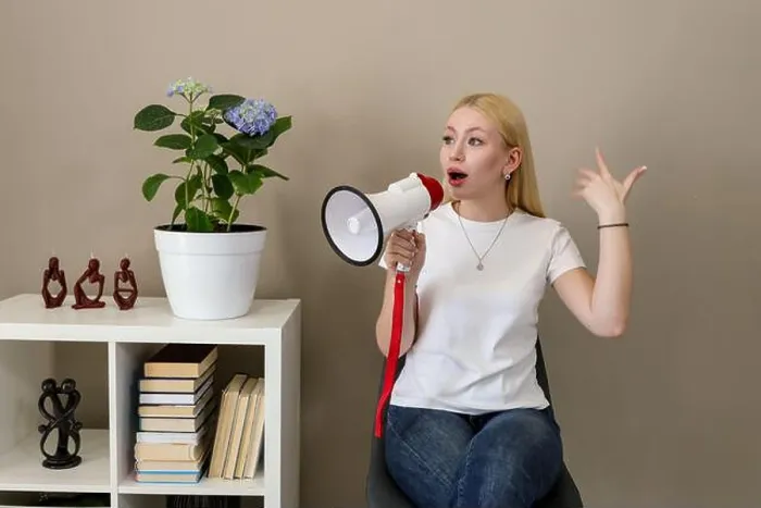 Framed Print : Blonde woman in casual white t-shirt and jeans gestures passionately while speaking into a red-and-white megaphone Framed Print : Blonde woman in casual white t-shirt and jeans gestures passionately while speaking into a red-and-white megaphone