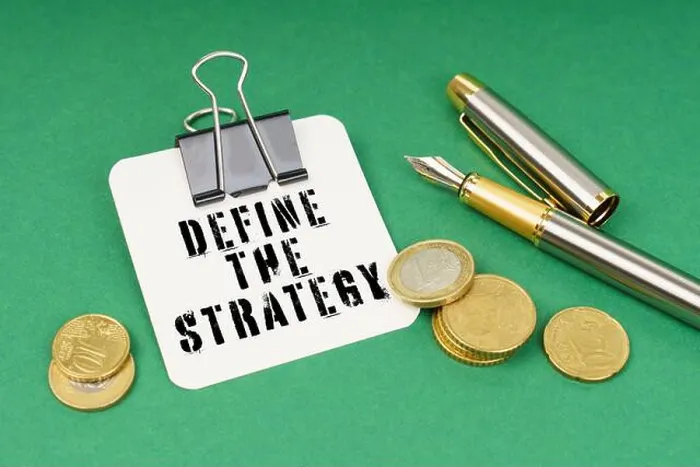 Framed Print : Business and finance concept. On a green surface, a pen, coins and a notepad with the inscription - Define The Strategy Framed Print : Business and finance concept. On a green surface, a pen, coins and a notepad with the inscription - Define The Strategy