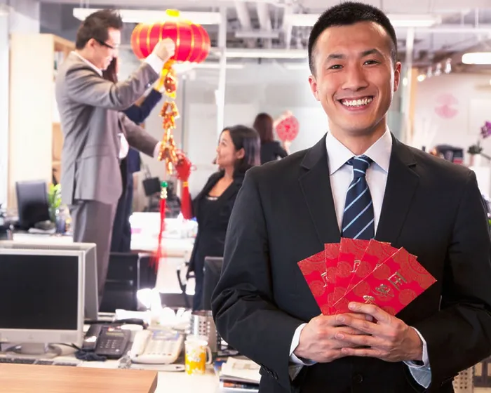 Framed Print : Businessman holding red envelopes and coworkers hanging decorations for Chinese new year