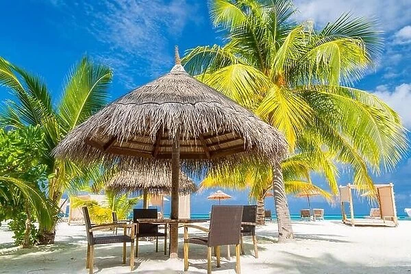 Cafe on the beach, ocean and sky as tropical landscape. Chairs with table under palm parasol. Exotic summer outdoor restaurant family vacation concept