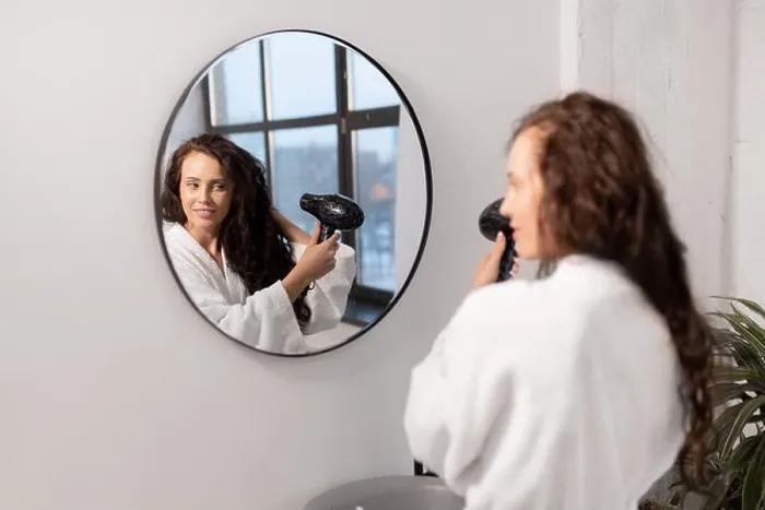 Framed Print : Charming young female with hair-dryer taking care of her dark long wavy hair Framed Print : Charming young female with hair-dryer taking care of her dark long wavy hair