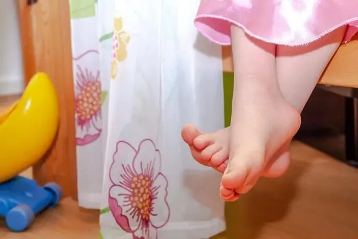 Framed Print : Close-up of little girl feet while sitting on bed Framed Print : Close-up of little girl feet while sitting on bed