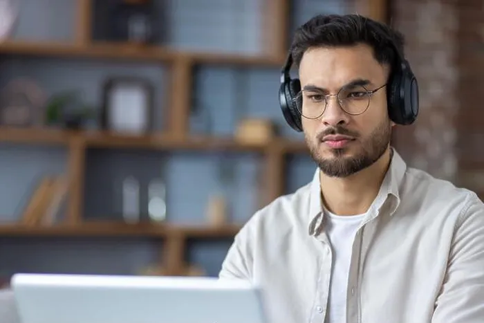 Framed Print : Close-up photo of a serious and focused young Indian man wearing headphones working and studying on a laptop at home Framed Print : Close-up photo of a serious and focused young Indian man wearing headphones working and studying on a laptop at home