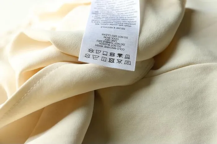 Framed Print : Clothing label with care instructions on beige garment, closeup Framed Print : Clothing label with care instructions on beige garment, closeup
