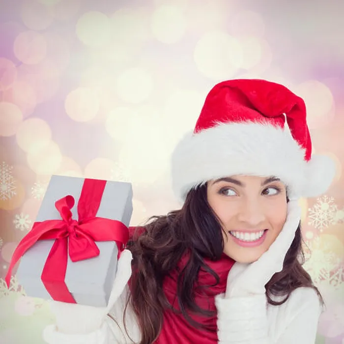 Framed Print : Composite image of surprised brunette in santa hat holding gift Framed Print : Composite image of surprised brunette in santa hat holding gift