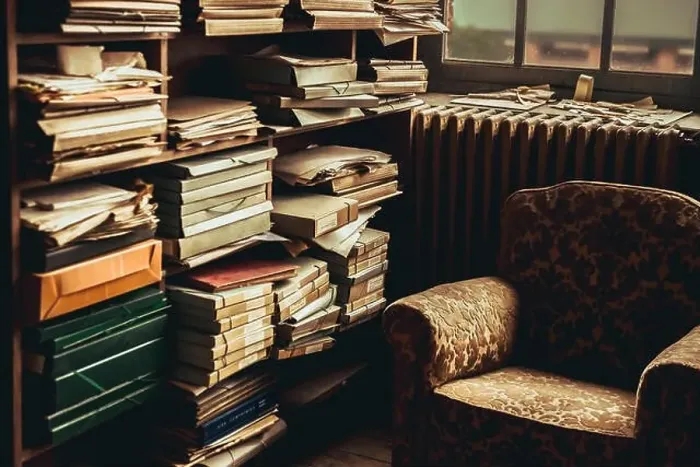 Framed Print : Composition of vintage armchair near shelves with piles of documents in room Framed Print : Composition of vintage armchair near shelves with piles of documents in room