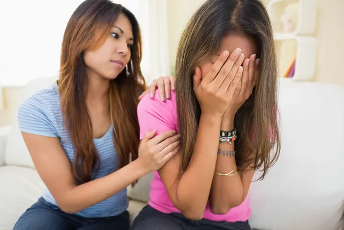 Framed Print : Crying woman sitting on a white couch being consoled by her sister Framed Print : Crying woman sitting on a white couch being consoled by her sister
