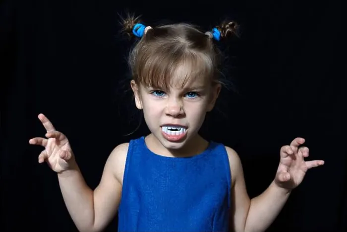 Framed Print : cute little vampire girl in blue dress with big fangs making scary faces at All Hallows Eve party on black background