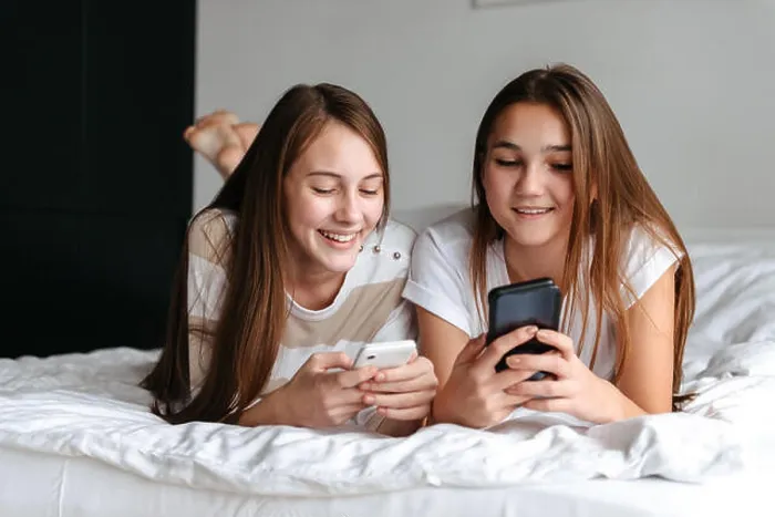 Framed Print : Two cute smiling teengae girls laying on bed, holding mobile phones at home Framed Print : Two cute smiling teengae girls laying on bed, holding mobile phones at home