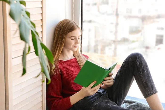 Framed Print : Cute teenage girl reading book on window sill at home Framed Print : Cute teenage girl reading book on window sill at home