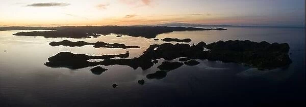 Dawn illuminates the serene waters surrounding limestone islands in Raja Ampat, Indonesia. This region is known for its high marine biodiversity
