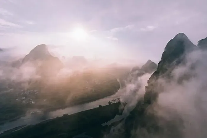 Framed Print : Drone view of calm river and rocky dark mountains in morning mist with flowing clouds under bright sky and sun Framed Print : Drone view of calm river and rocky dark mountains in morning mist with flowing clouds under bright sky and sun