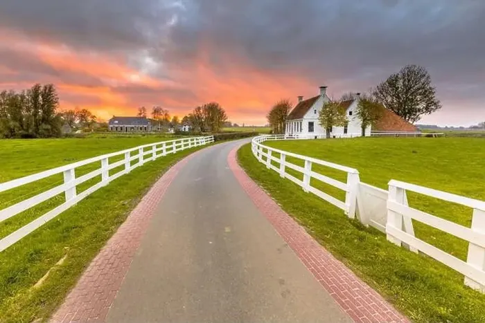 Framed Print : Dutch Countryside landscape with historical houses in evening along a curved road with white fence in the country Framed Print : Dutch Countryside landscape with historical houses in evening along a curved road with white fence in the country