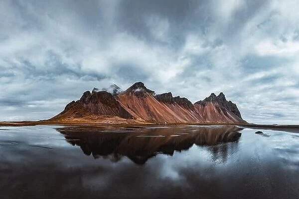 Famous Stokksnes mountains on Vestrahorn cape in southeastern Icelandic coast. The epic sky reflected in the clear water. Iceland island