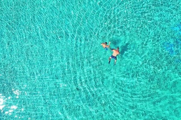 Father and son snorkels through tropical, turquoise waters, aerial view
