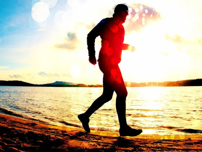 Framed Print : Film grain effect. Tall man with sunglass and dark cap is running on the beach at sunset
