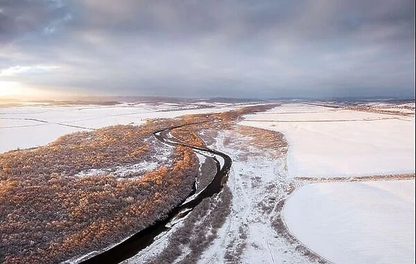 Flight through majestic river, frozen forest and frosty winter fields at sunrise time. Landscape photography