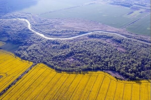 Flight through majestic river, lush green forest and blooming yellow rapeseed fields at sunset time. Landscape photography
