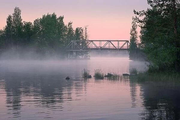 Foggy summer landscape and old iron bridge with beautiful calm lake at summer night in Finland