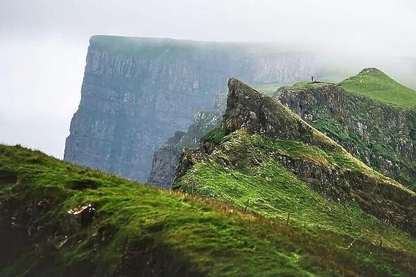 Foggy view of gorgeous mountains of Mykines island with tourist on high viewpoint. Faroe islands, Denmark. Landscape photography
