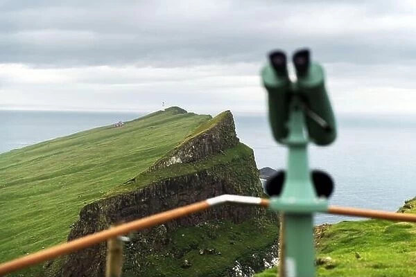 Foggy view of old lighthouse from viewpoint with tourist binoculars on the Mykines island, Faroe islands, Denmark. Landscape photography