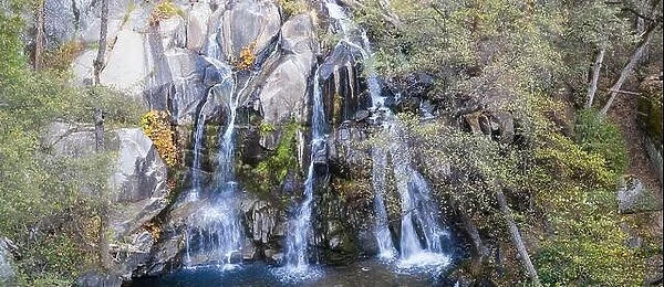 Freshwater from a stream tumbles down a rocky cliff face forming a beautiful waterfall in a wild California forest