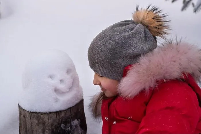 Framed Print : A girl in a winter hat and a red jacket with a small snowman in the snow. The concept of winter fun Framed Print : A girl in a winter hat and a red jacket with a small snowman in the snow. The concept of winter fun