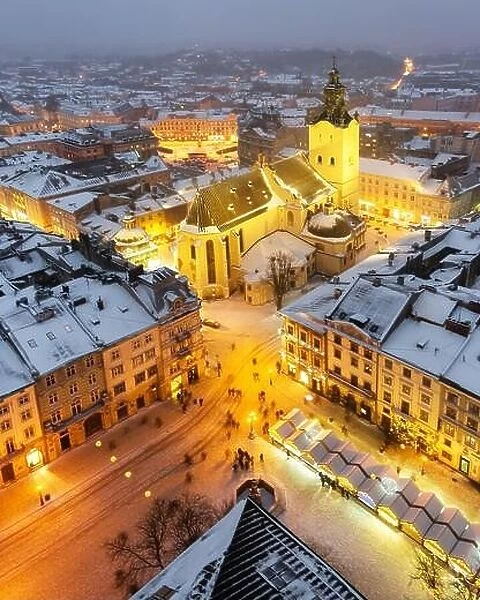 Gorgeus cityscape of winter Lviv city with roofs covered by snow from top of town hall, Ukraine, Europe. Latin Cathedral glowing by city lights