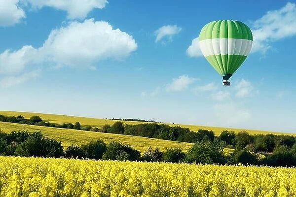 Green balloon under yellow rape field on blue sky background. Landscape photography