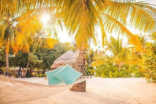 Hammock and pillows between two palm trees on the beach during sunset time. Tranquility and calmness, summer beach vacation travel view, sun rays
