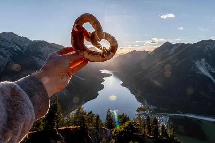 Framed Print : Hand holding Bavarian pretzel in front of Alpine panorama, view from Schonjochl to Plansee, Tyrol, Austria Framed Print : Hand holding Bavarian pretzel in front of Alpine panorama, view from Schonjochl to Plansee, Tyrol, Austria