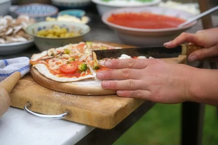 Framed Print : Hands cutting freshly baked pizza on a rustic wooden board Framed Print : Hands cutting freshly baked pizza on a rustic wooden board
