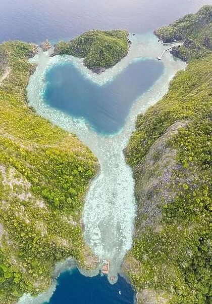 Healthy coral reefs surround a heart-shaped lagoon in Raja Ampat, Indonesia. This amazing tropical region is famous for its high marine biodiversity