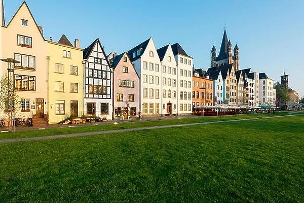 Houses and park in Cologne, Germany. Many of them are colourful, they are facing a public park with green grass and some trees. There is a Cologne bel