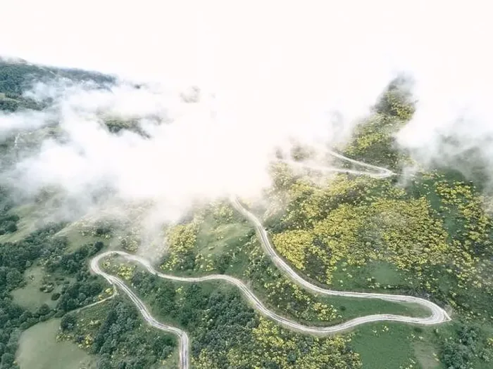 Framed Print : image taken with a drone of the long road with many curves under the fog on the slope of the green mountain between Framed Print : image taken with a drone of the long road with many curves under the fog on the slope of the green mountain between