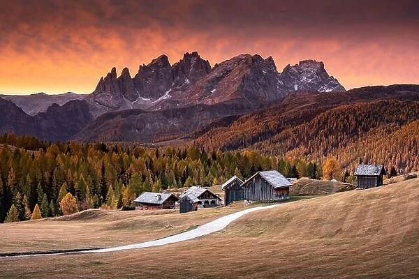 Incredible red sunset at Fuchiade valley in Italian Dolomites countryside. Wooden huts, orange larches forest