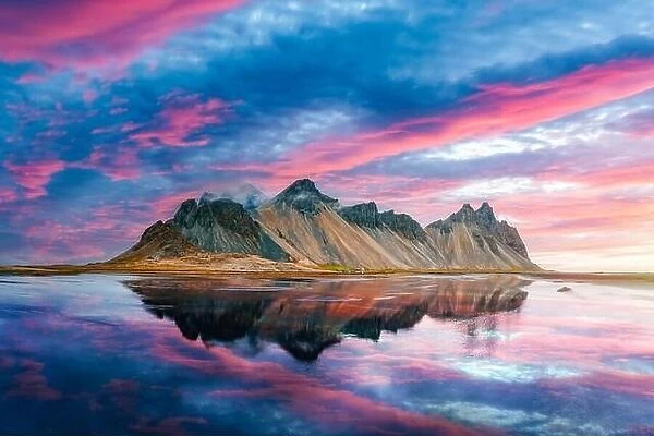 Incredible Stokksnes mountains on Vestrahorn cape in southeastern Icelandic coast during sunset. The epic pink sky reflected in the clear water