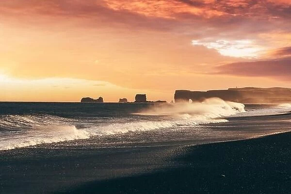 Incredible sunset view on stormy Atlantic ocean on Black Beach, Vik, Iceland. Big waves, orange sky and dark rocks. Landscape photography
