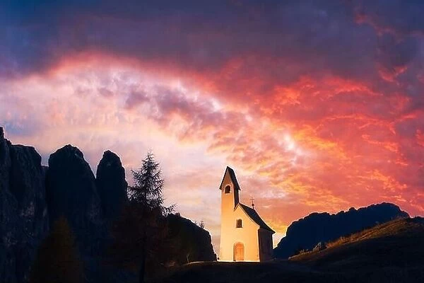Incredible view on small iIlluminated chapel - Kapelle Ciapela on Gardena Pass, Italian Dolomites mountains. Colorful sunset in Dolomite Alps, Italy