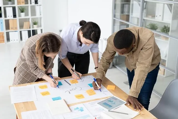 Framed Print : Three intercultural colleagues with highlighters bending over table with papers Framed Print : Three intercultural colleagues with highlighters bending over table with papers