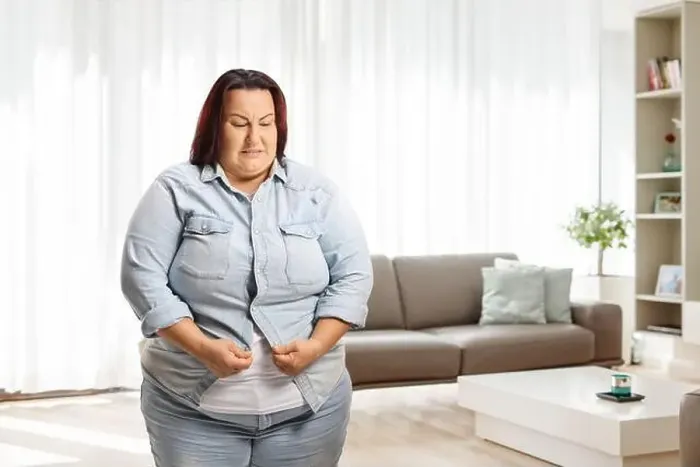Framed Print : Irritated overweight woman at home trying to button a denim shirt Framed Print : Irritated overweight woman at home trying to button a denim shirt