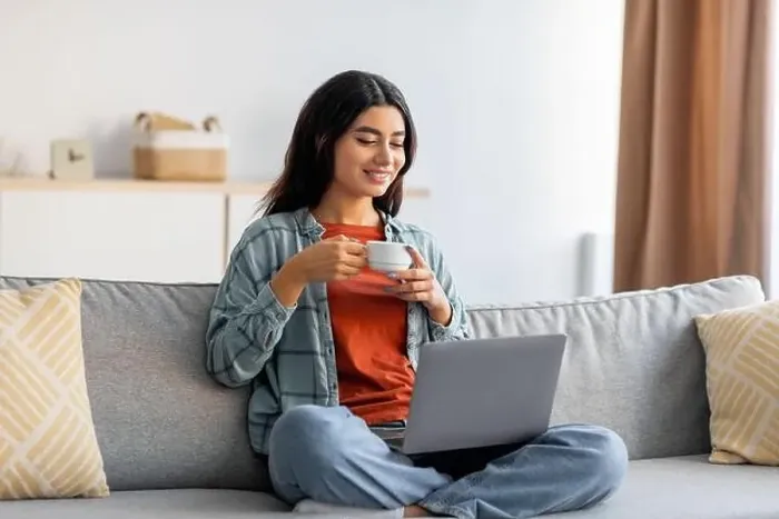 Framed Print : Full length of beautiful young Arab woman sitting cross legged on couch, working on laptop, drinking coffee at home Framed Print : Full length of beautiful young Arab woman sitting cross legged on couch, working on laptop, drinking coffee at home