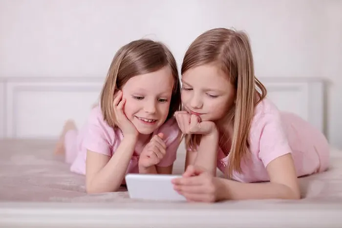 Framed Print : Two little girls (sisters) in pink pajamas on the bed watching a smartphone and reading an e-book. Selective focus